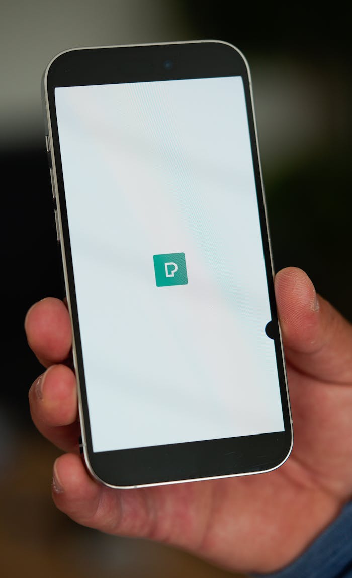 A person holds a smartphone displaying a green app icon on the screen.